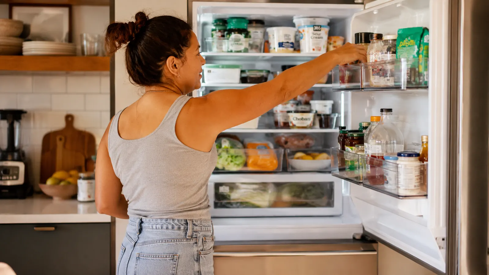 Open refrigerator with clear bins organizing produce, leftovers, and condiments on every shelf