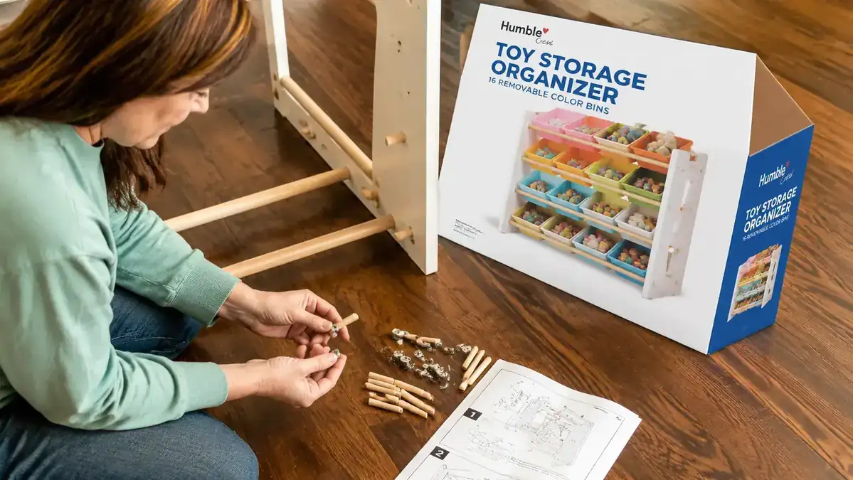 Close-up of the Humble Crew organizer frame joints and peg connectors during assembly, hardware pieces laid out on a wood floor