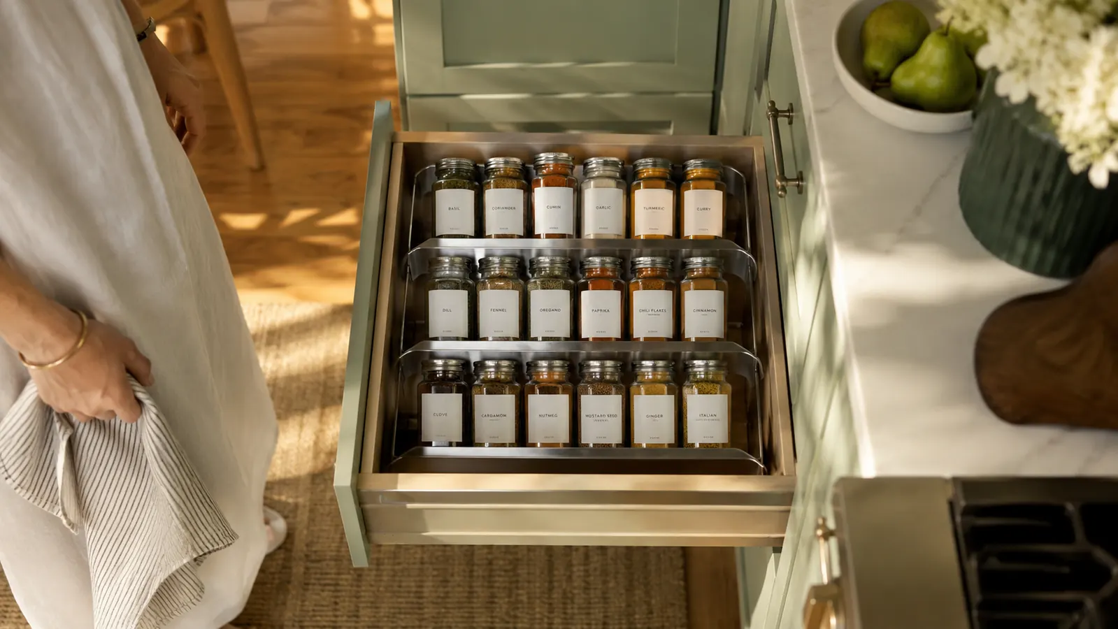 Open kitchen drawer showing a 4-tier steel spice rack with neatly arranged spice jars in a bright, organized kitchen